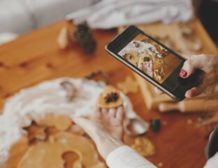 Woman holding a phone and taking photos of gingerbread Christmas cookies on a messy table flat lay. Instagram photo, social media, and blog. Holiday preparations