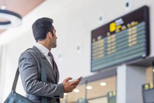 Businessman with smart phone checking arrival departure board