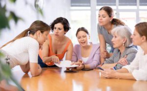 Women of different ages examine documents while sitting at table in office